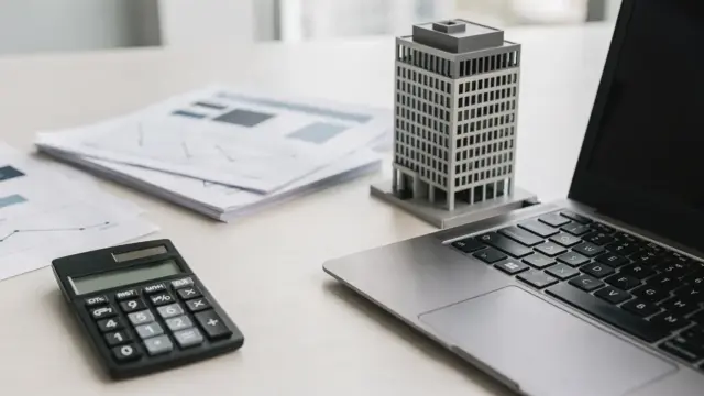 Büro-Desk mit Unterlagen, Taschenrechner und Modellhaus zum Thema Sicherheiten beim Firmenkredit