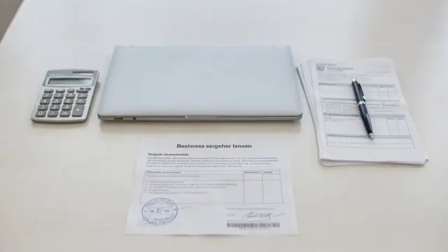 Unterlagen zur Gewerbeanmeldung auf einem Schreibtisch mit Laptop, Formularen und Stempel.